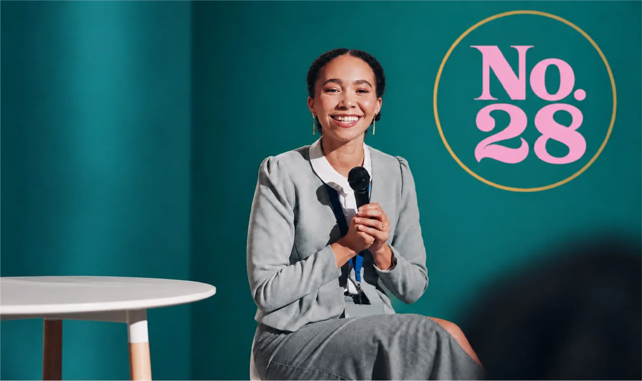 A speaker smiling on stage in front of the No.28 sign